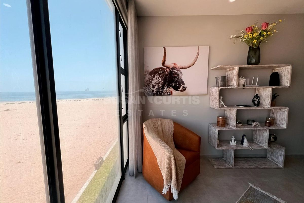 A bright living area featuring large floor-to-ceiling windows with direct views of the beach and ocean.