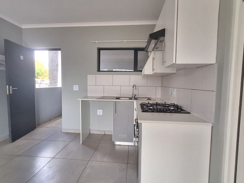 Modern kitchen featuring built-in cabinetry, a gas hob with extractor fan, stainless steel sink, and neutral tiled flooring.