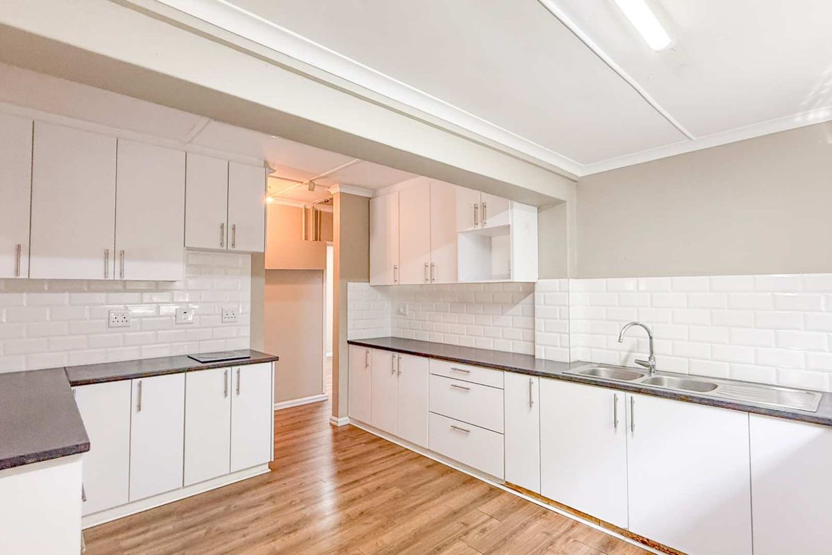 A bright, modern kitchen featuring white cabinetry, subway tile backsplash, dark countertops, and wood-look flooring.