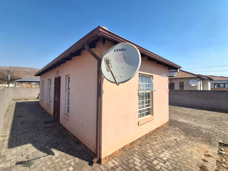 Rear exterior view of the property featuring a paved yard, security gate, and satellite dish installation.