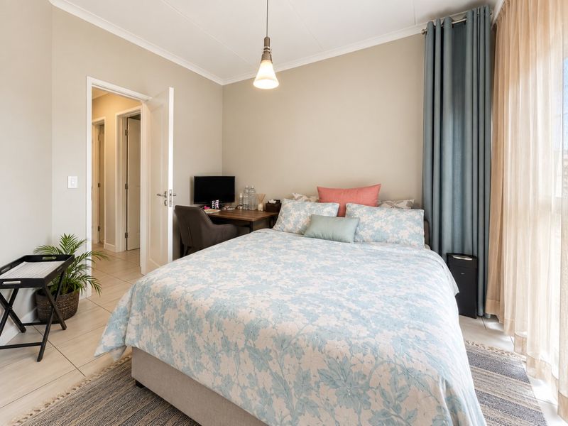A well-maintained bedroom featuring neutral wall tones, tiled flooring, and a large window with floor-to-ceiling curtains, providing a bright and comfortable living space.