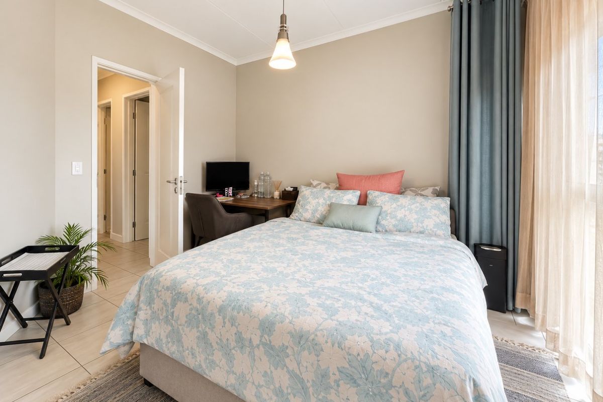 A well-maintained bedroom featuring neutral wall tones, tiled flooring, and a large window with floor-to-ceiling curtains, providing a bright and comfortable living space.