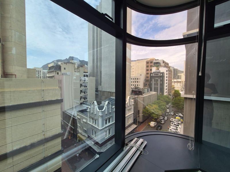 A high-rise office view featuring large curved windows overlooking the surrounding city architecture and streetscape.