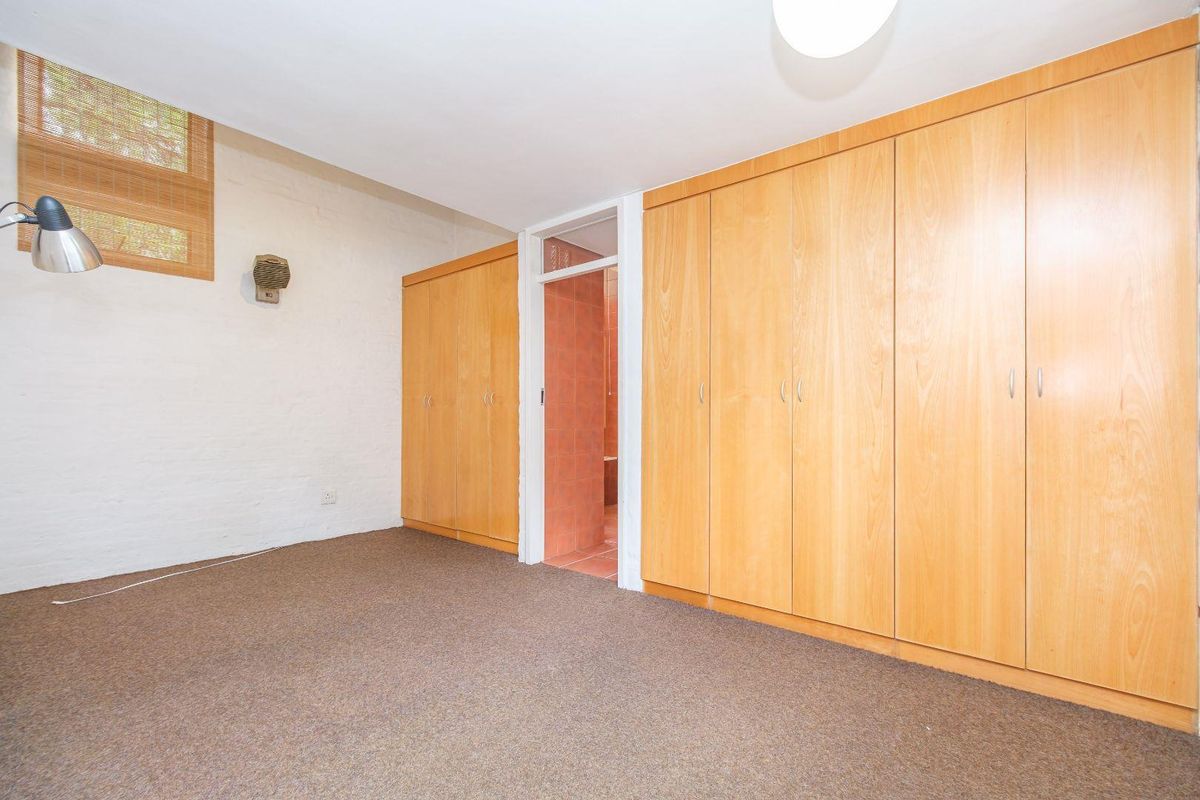 A bedroom featuring built-in wooden cabinetry, carpeted flooring, and an adjoining tiled bathroom area.