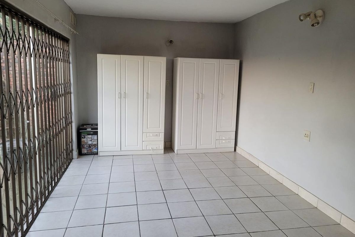A bedroom featuring tiled flooring, a security gate, and wall-mounted lighting, providing a functional space ready for personalization.