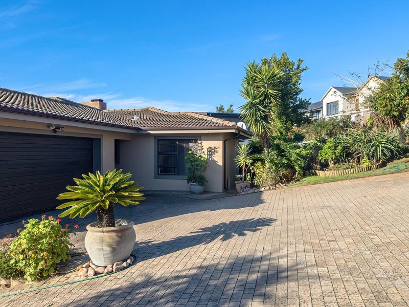 Front exterior view of the house featuring a paved driveway, garage access, and established garden landscaping under a clear blue sky.