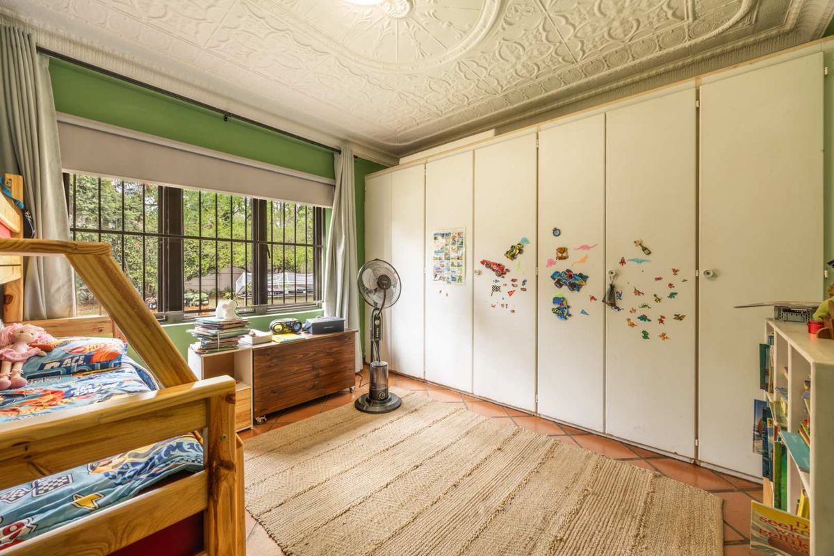 A bedroom featuring built-in cupboards, classic pressed metal ceiling detailing, terracotta floor tiles, and security bars on the window.