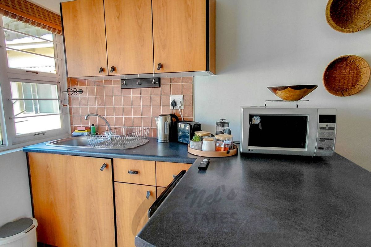 A compact kitchen area featuring wooden cabinetry, dark laminate countertops, a stainless steel sink, and a tiled backsplash.