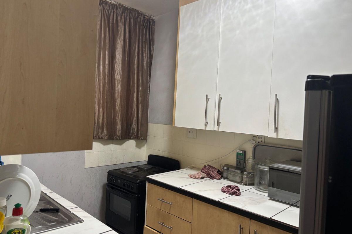 A compact kitchen featuring built-in cabinetry, tiled countertops, a stainless steel sink, and a freestanding stove, offering a functional layout with potential for modernization.