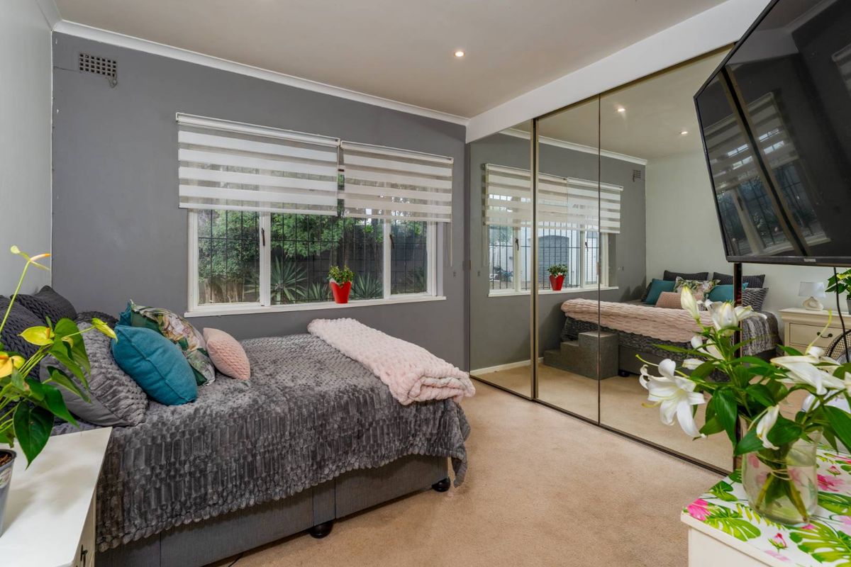 A well-maintained bedroom featuring neutral carpeting, grey accent walls, and large floor-to-ceiling mirrored built-in wardrobes that enhance the sense of space.