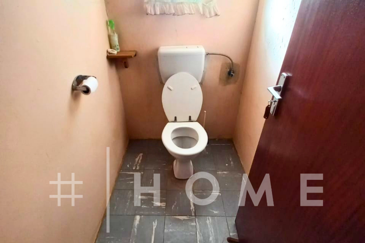 A compact bathroom featuring a standard toilet, tiled flooring, and a wooden door, requiring cosmetic updates to improve its overall condition.