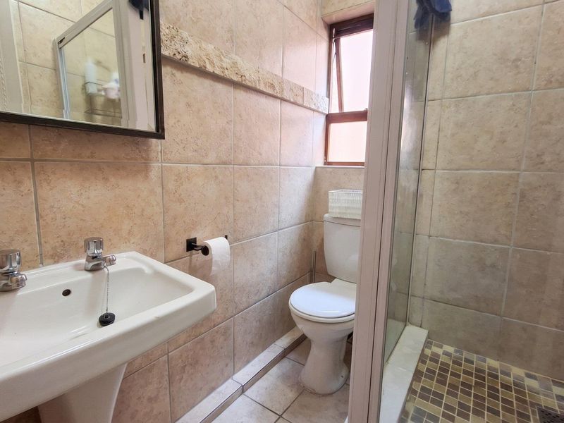 A functional bathroom featuring a pedestal basin, toilet, and a glass-enclosed shower with neutral wall and floor tiling.