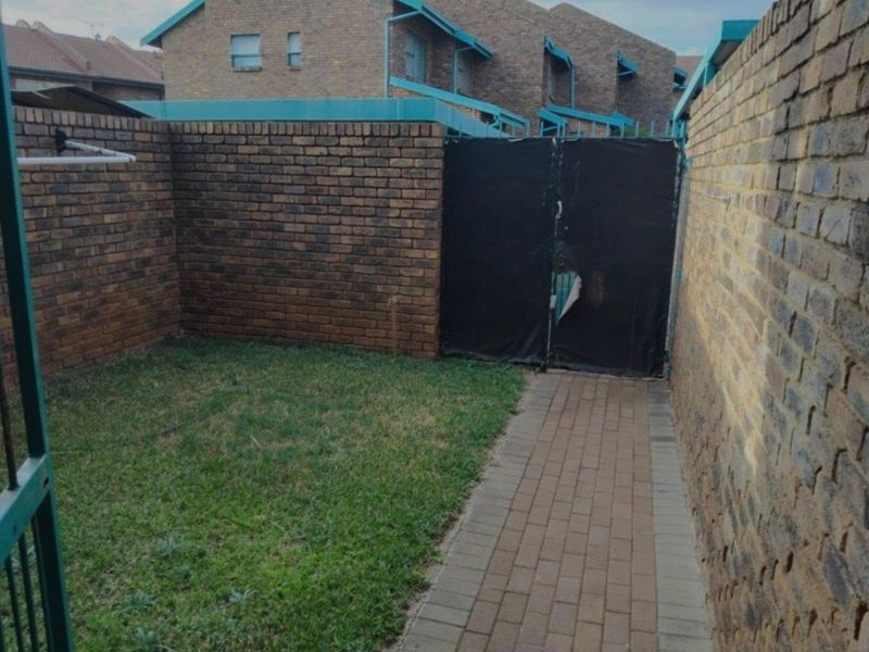 A private rear courtyard featuring a brick boundary wall, paved walkway, and a small lawn area with a gated entrance.