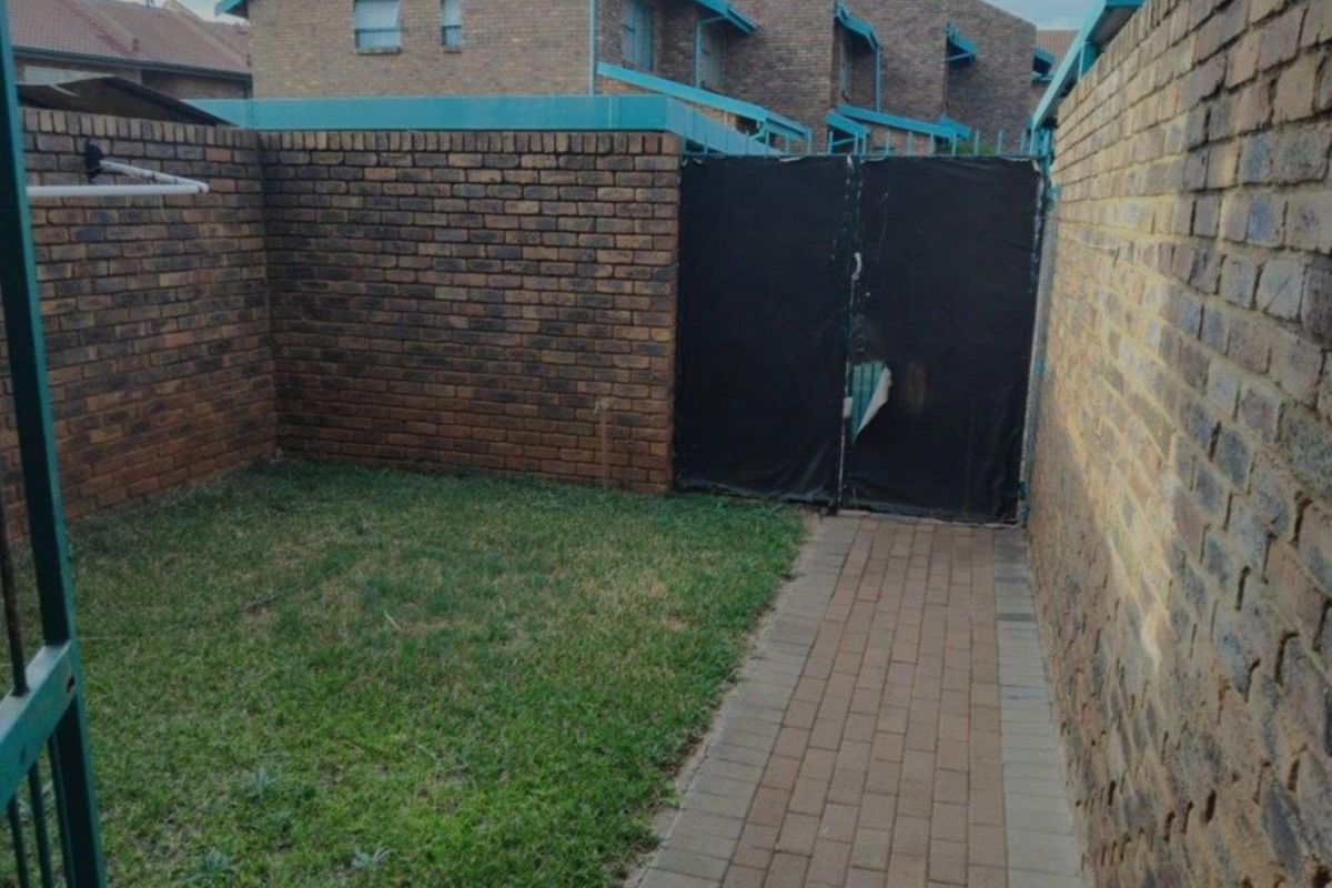 A private rear courtyard featuring a brick boundary wall, paved walkway, and a small lawn area with a gated entrance.