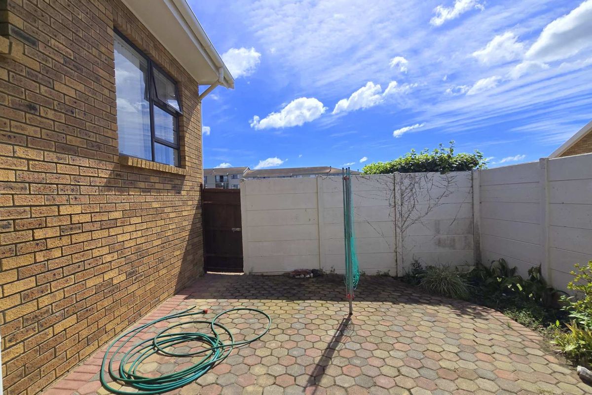 A private rear courtyard featuring paved flooring, face brick exterior walls, and a secure precast concrete boundary wall with a side access gate.