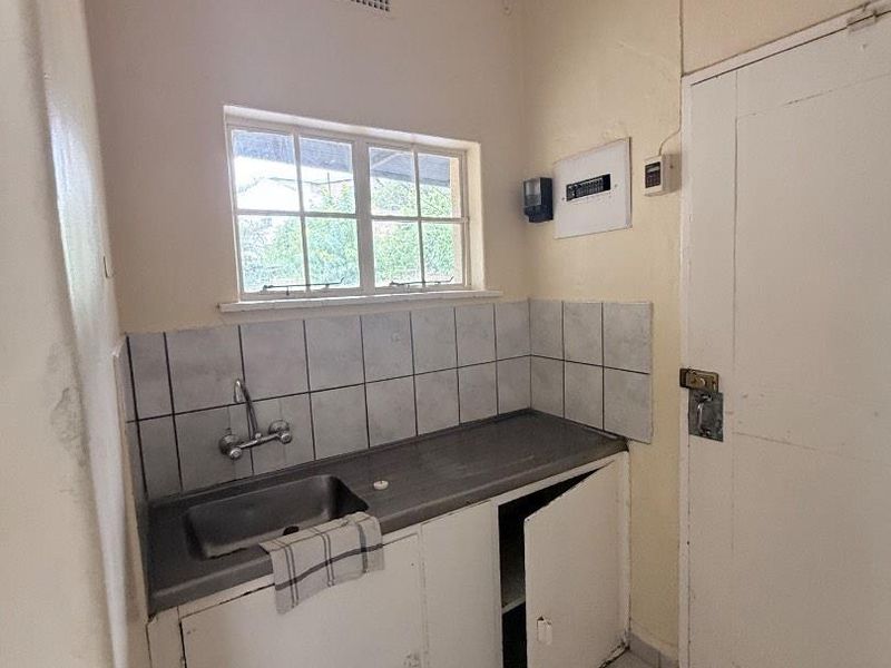 A functional laundry area featuring a stainless steel sink, tiled splashback, and built-in cabinetry, requiring minor cosmetic updates.