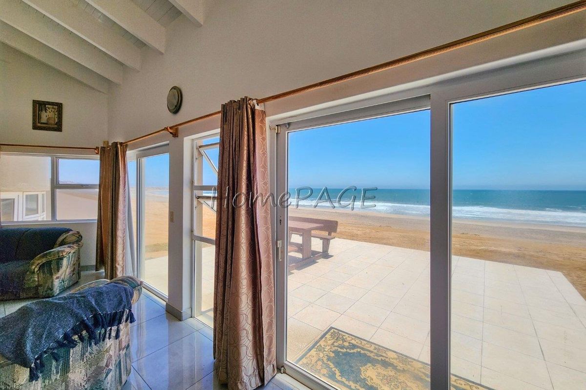Living area featuring large sliding glass doors that open onto a tiled patio with direct beach and ocean views.