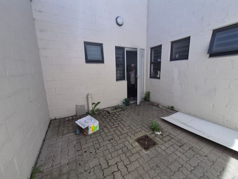 A paved rear courtyard area featuring concrete block walls, drainage, and access to the building interior via a single door.