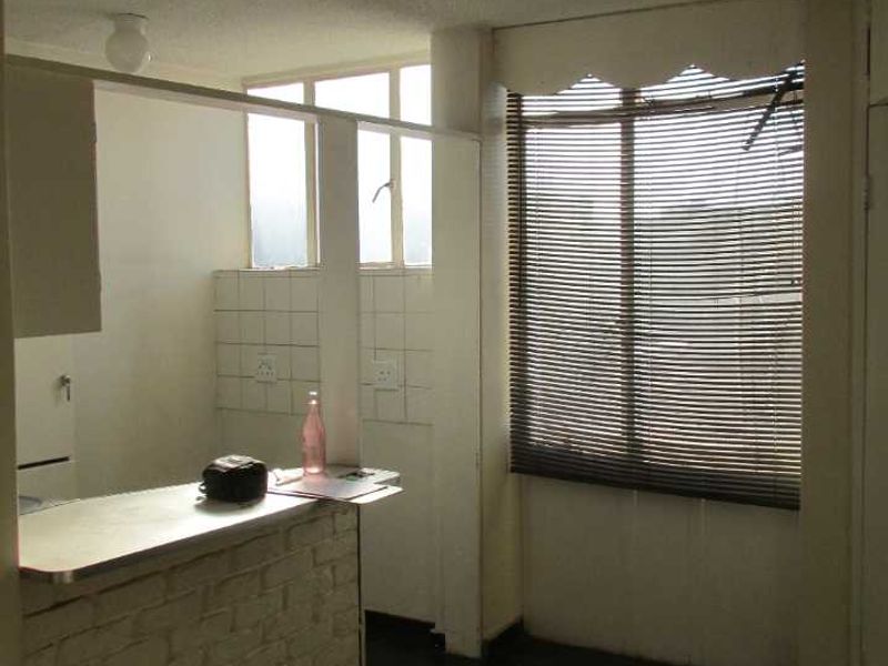 Open plan living and kitchen area featuring a brick breakfast bar, tiled flooring, and large windows with venetian blinds.