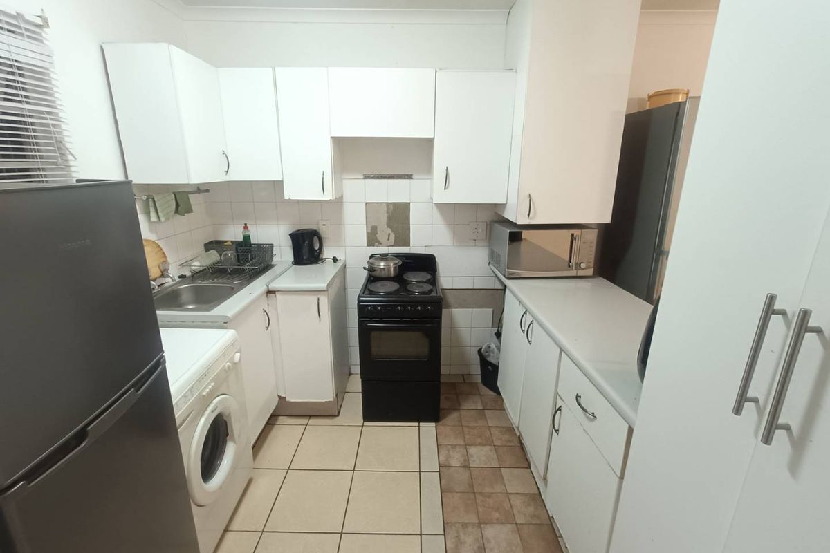 A functional kitchen featuring white built-in cabinetry, laminate countertops, a tiled backsplash, and a freestanding stove with tiled flooring.