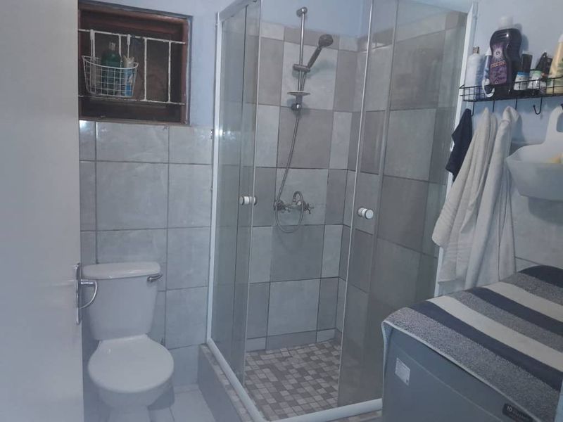 A functional bathroom featuring a glass shower enclosure, standard toilet, and tiled finishes, requiring cosmetic updates to improve its overall aesthetic appeal.