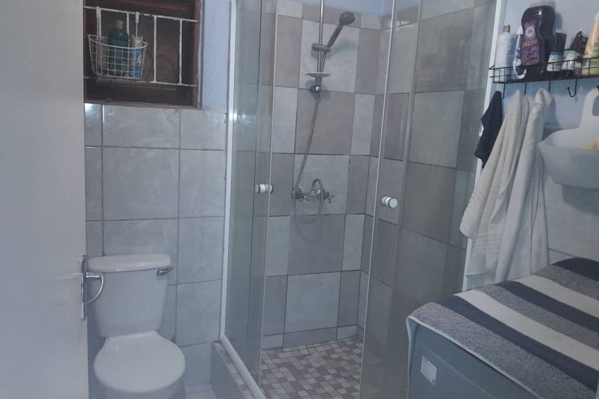 A functional bathroom featuring a glass shower enclosure, standard toilet, and tiled finishes, requiring cosmetic updates to improve its overall aesthetic appeal.