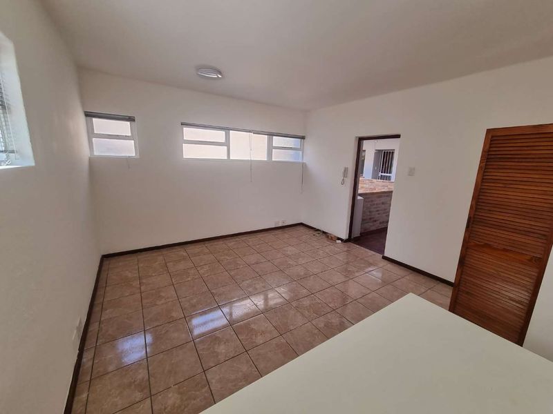 An empty living area featuring tiled flooring, built-in wooden louvered storage, and natural light from horizontal windows.