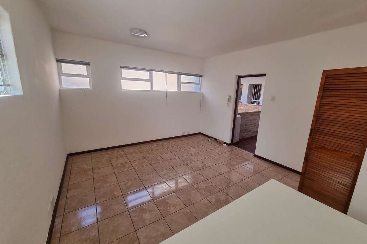 An empty living area featuring tiled flooring, built-in wooden louvered storage, and natural light from horizontal windows.