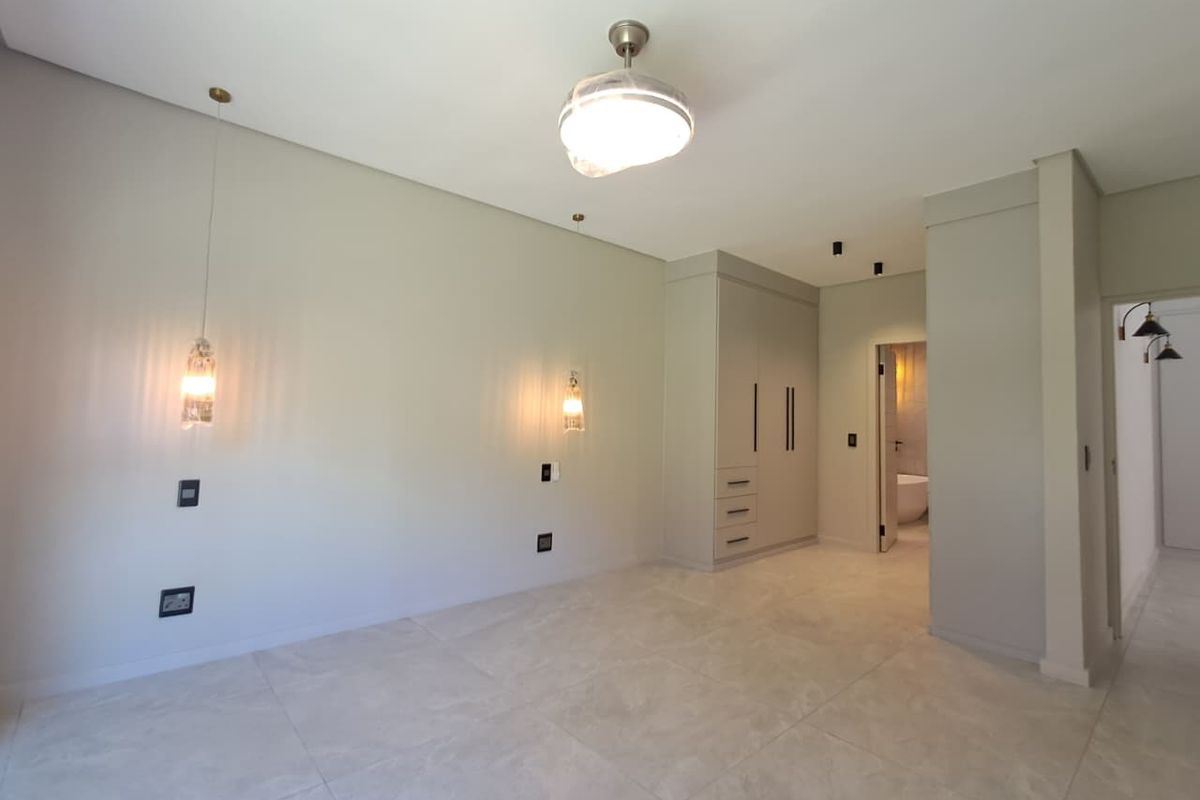 Spacious bedroom featuring neutral tiled flooring, built-in cabinetry, modern pendant lighting, and direct access to an en-suite bathroom.