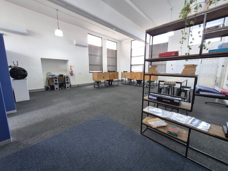 Spacious open-plan office area featuring high ceilings, large windows for natural light, air conditioning, and carpeted flooring.