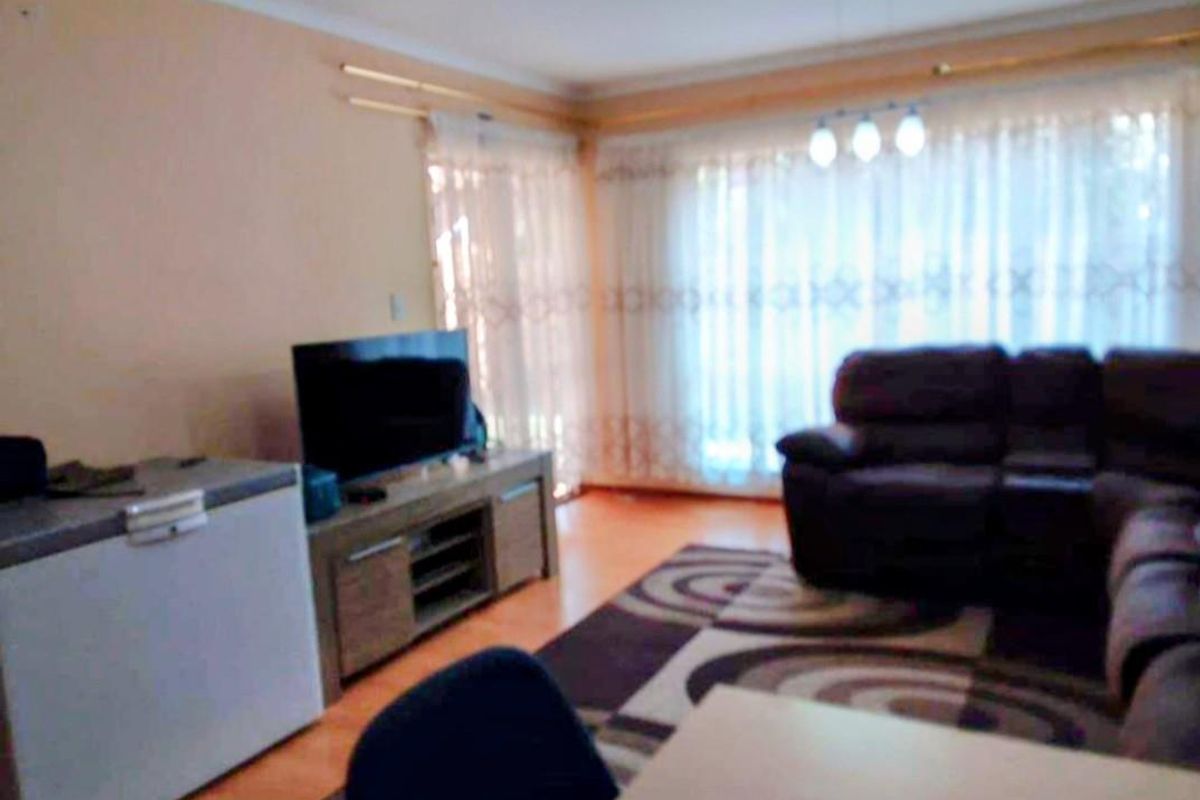 A living room area featuring laminate flooring, large windows with curtains, and coved ceiling detailing.