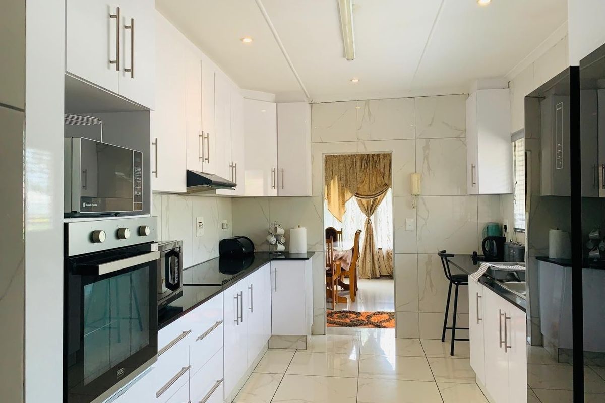 Modern galley-style kitchen featuring gloss white cabinetry, black stone countertops, marble-look wall and floor tiles, and integrated built-in appliances.