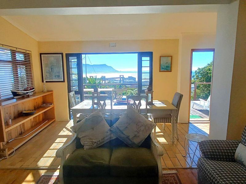Open-plan living and dining area featuring wooden flooring, built-in shelving, and large sliding doors opening to an outdoor patio with scenic views.