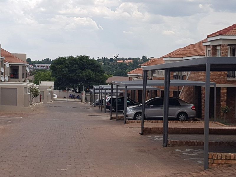 Exterior view of an apartment complex featuring a paved driveway and covered carport parking bays with brick building facades.