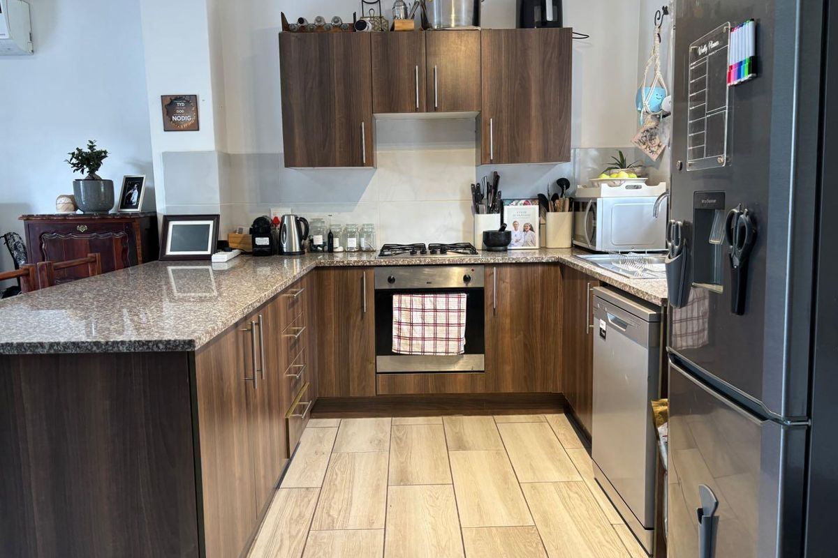 A functional kitchen featuring dark wood-look cabinetry, granite countertops, a built-in oven with gas hob, and light-toned tiled flooring.