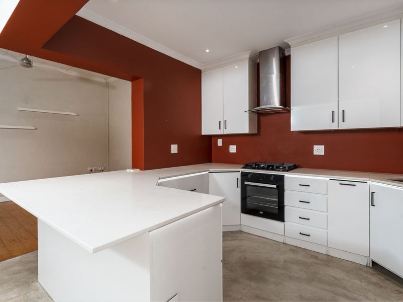 A modern kitchen featuring white cabinetry, quartz countertops, a built-in oven with gas hob, and polished concrete flooring.