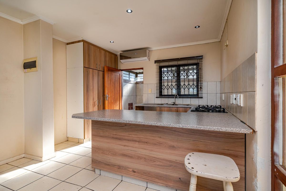A functional kitchen featuring wood-look cabinetry, laminate countertops, a gas hob, and tiled flooring, offering a practical layout for daily meal preparation.