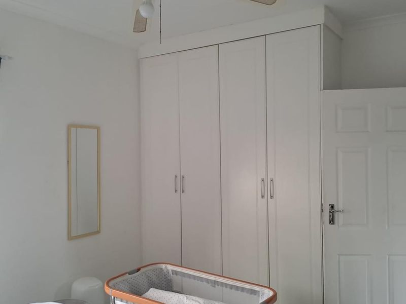 A bedroom featuring white built-in cupboards, a ceiling fan, and a classic panel door, providing functional storage and ventilation.