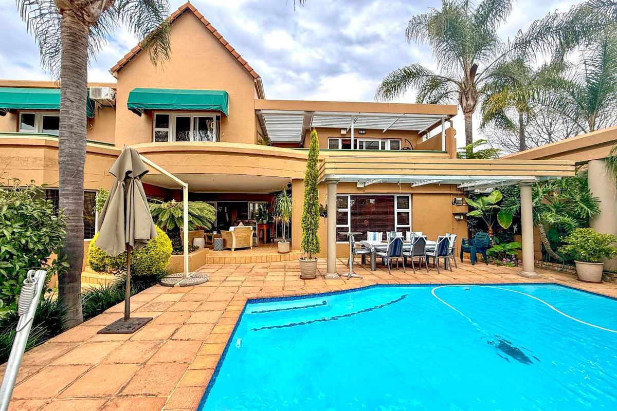 Rear exterior view of the house featuring a swimming pool, paved pool deck, covered patio area, and an upper-level balcony.