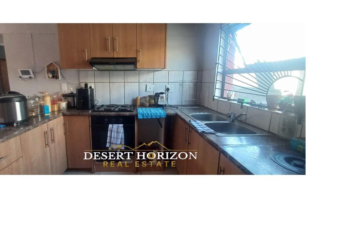 A functional kitchen featuring wooden cabinetry, laminate countertops, a built-in oven with hob, extractor fan, and a double basin sink.