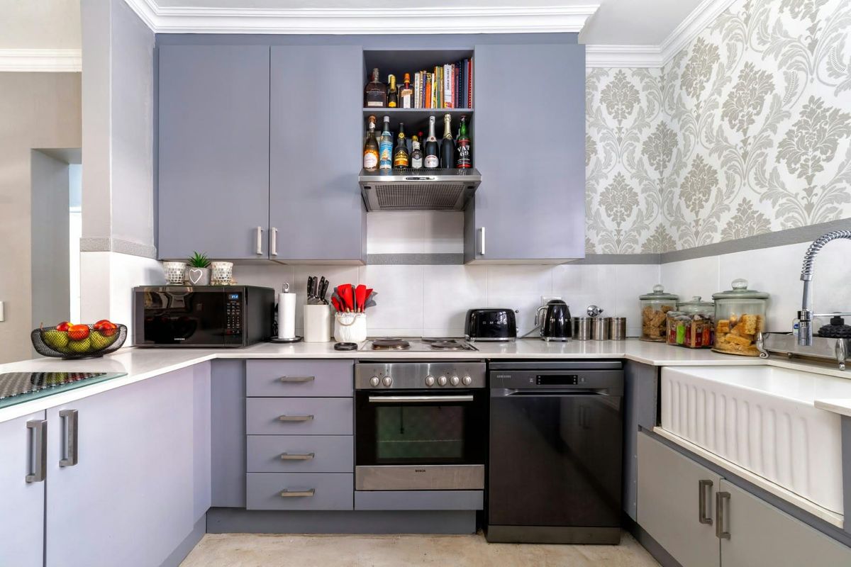 A well-maintained kitchen featuring grey cabinetry, a classic apron-front sink, built-in oven, electric hob, and decorative wallpaper, offering a functional and stylish cooking space.
