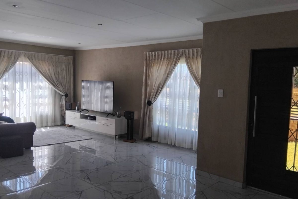 Spacious living room featuring polished marble-look floor tiles, recessed ceiling lighting, and large windows with curtains, providing a bright and modern atmosphere.