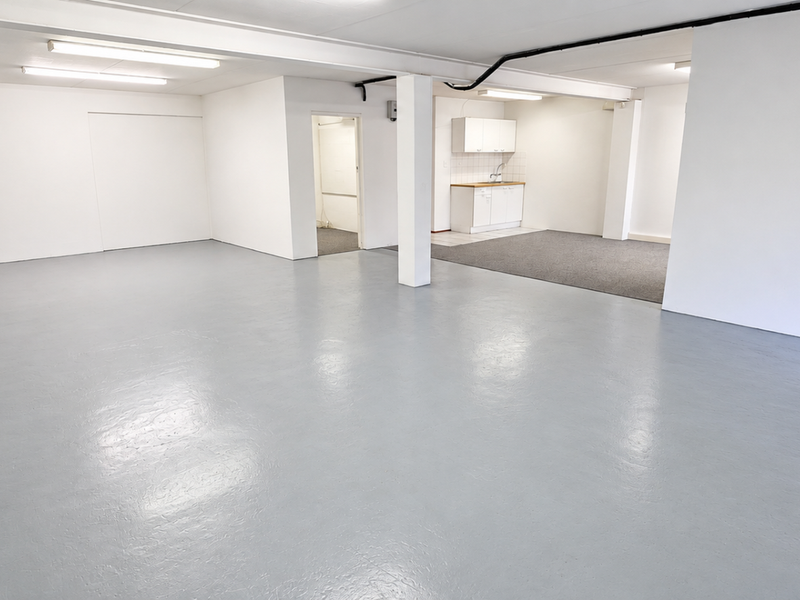 Spacious open-plan industrial area featuring durable epoxy flooring, bright fluorescent lighting, and a functional kitchenette with built-in cabinetry and sink.