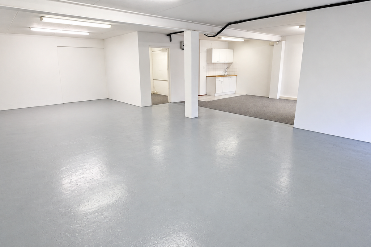 Spacious open-plan industrial area featuring durable epoxy flooring, bright fluorescent lighting, and a functional kitchenette with built-in cabinetry and sink.