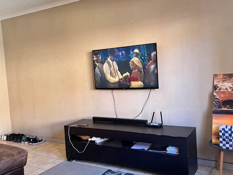 A living room area featuring tiled flooring and a wall-mounted television setup, requiring minor cosmetic updates to the wall finishes.