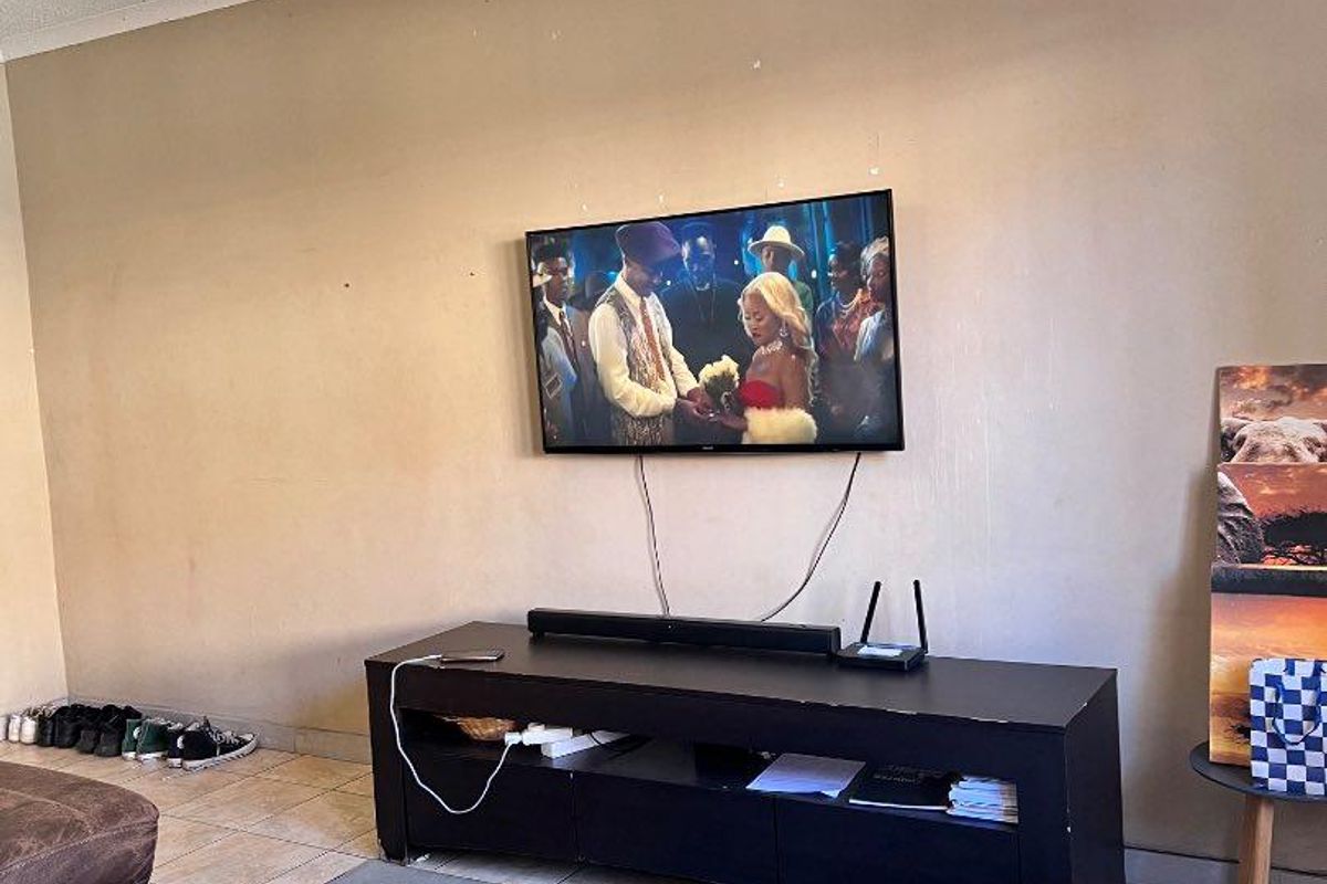 A living room area featuring tiled flooring and a wall-mounted television setup, requiring minor cosmetic updates to the wall finishes.