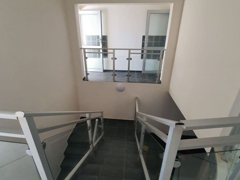 A bright hallway featuring a staircase with a modern glass and metal balustrade, leading to an upper landing area with tiled flooring.