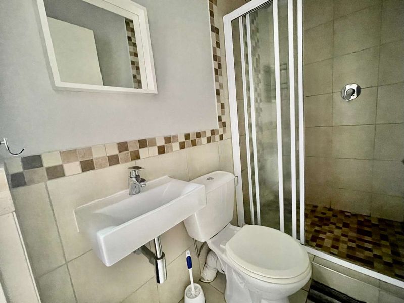 Compact bathroom featuring a wall-mounted basin, toilet, and a tiled shower enclosure with a sliding door.