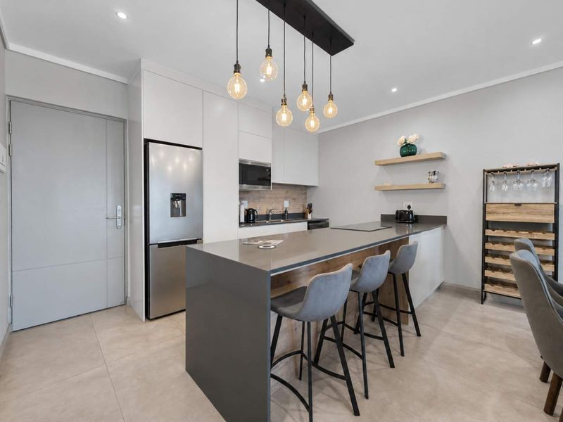 Modern kitchen featuring a large central island with stone countertops, sleek white cabinetry, built-in microwave, and stylish pendant lighting over the breakfast bar.