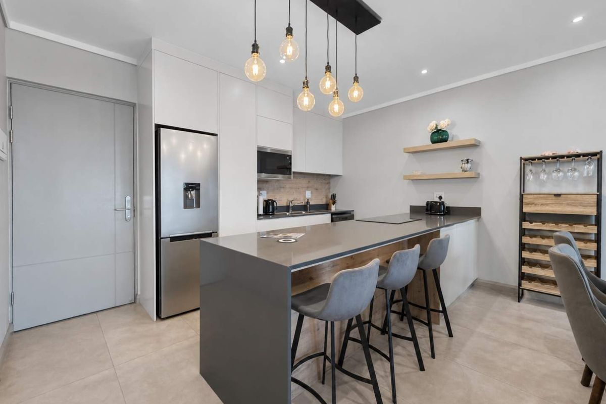 Modern kitchen featuring a large central island with stone countertops, sleek white cabinetry, built-in microwave, and stylish pendant lighting over the breakfast bar.